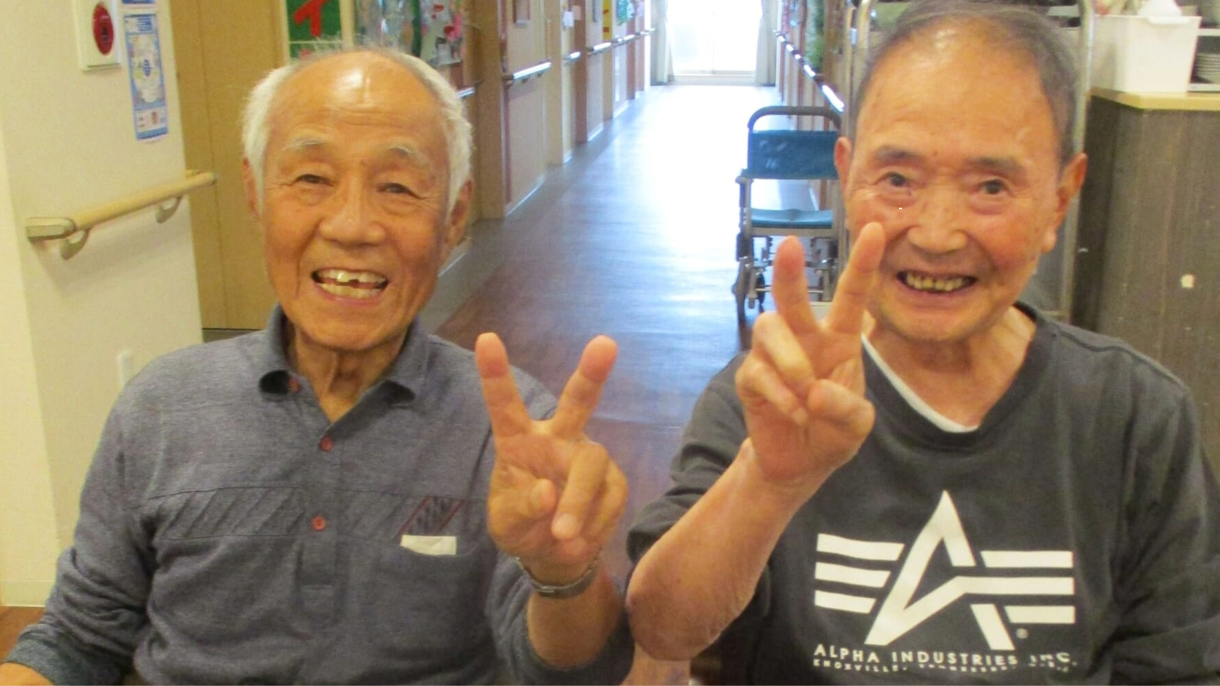 廊下で笑顔でポーズを取る入居者2名。施設内での日常生活風景。
