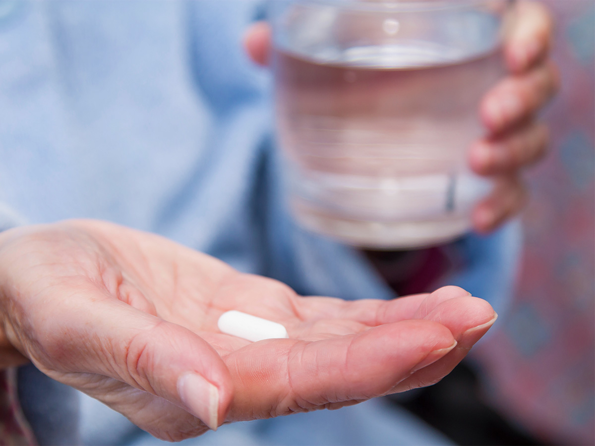 水入りのコップと薬を持つ人の手元