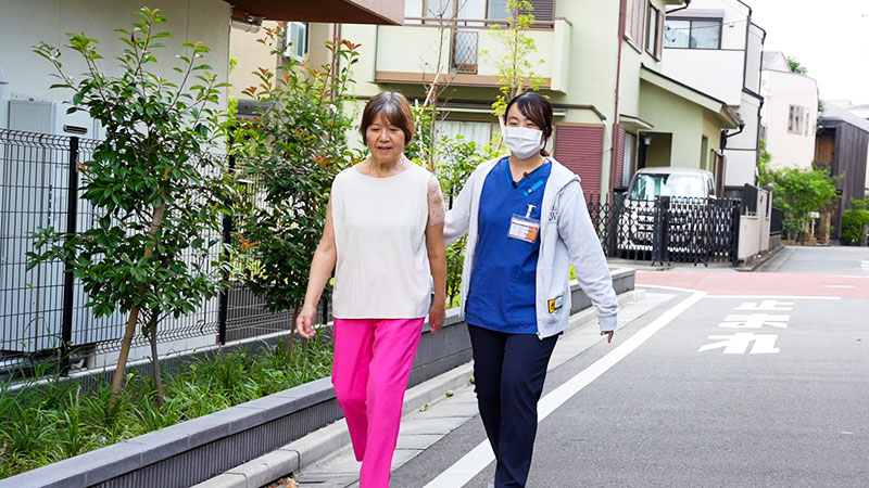 施設の周りを散歩する佐藤様と歩行補助をするリハビリ職員